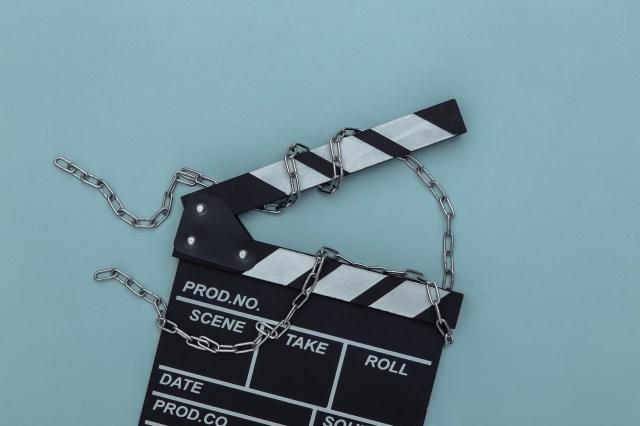 Movie clapperboard wrapped in steel chain on blue background. Ban on filmmaking. Top view