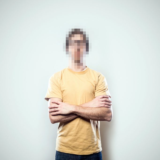 A portrait of a hipster young man from the waist up, whose face has been rendered unrecognizable by being pixelated.  A conceptual representation of individual identity protection.  Square crop with copy space on a a clean off-white background.
